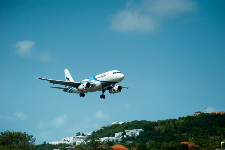 A passenger airplane descends for landing over lush hills in sunny Thailand.