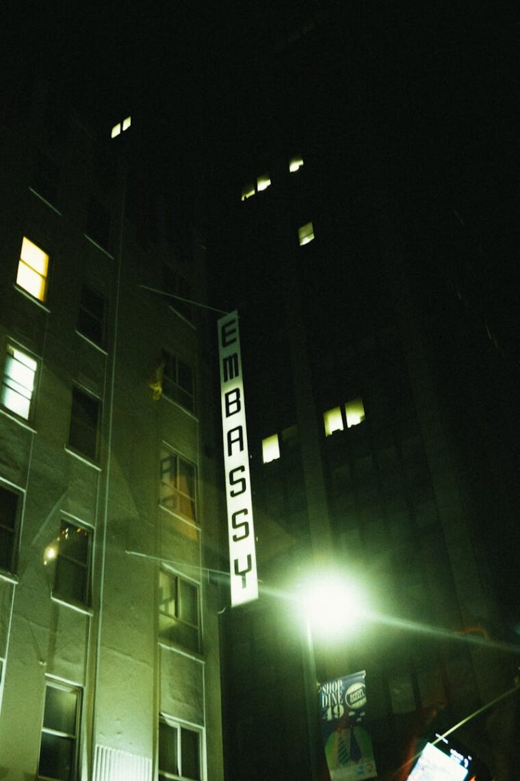 Nighttime view of a cityscape with an illuminated Embassy sign on a building.