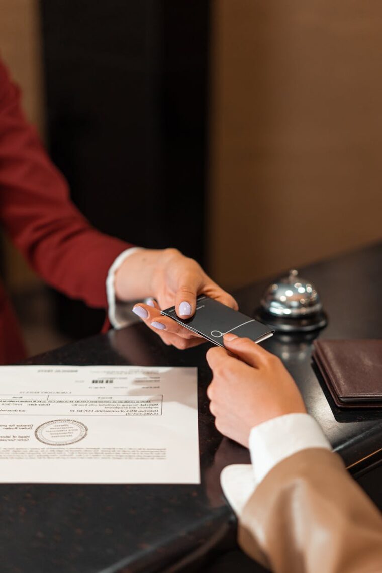 A hotel receptionist hands a key card to a guest over the counter, with documents visible.