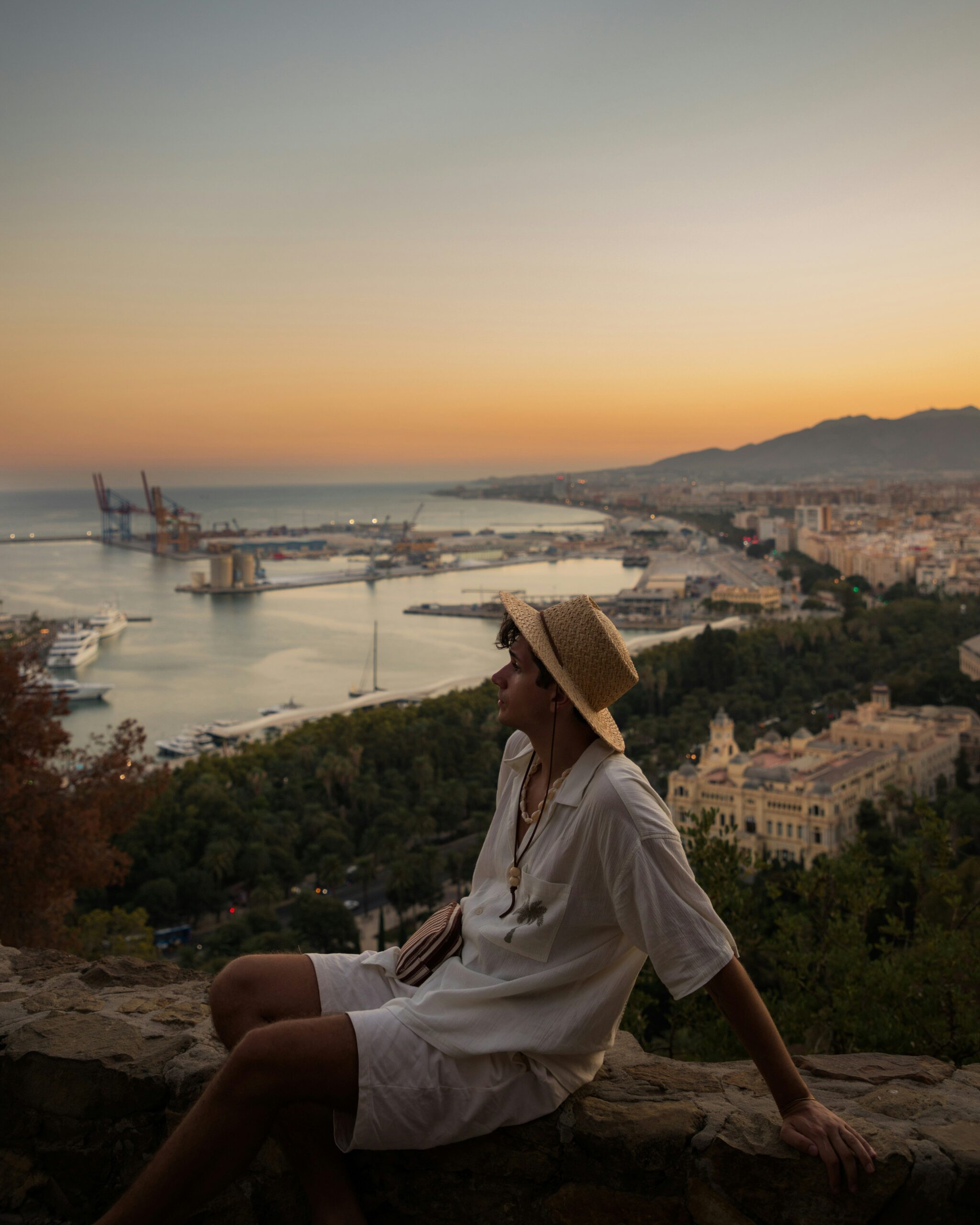 A woman sitting on top of a cliff overlooking a city