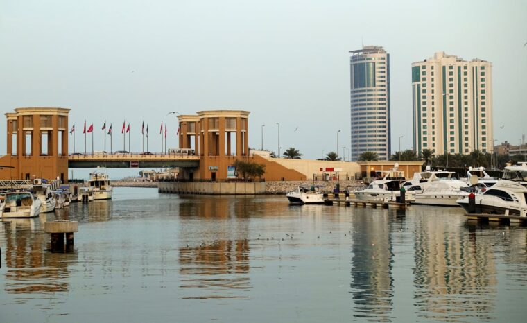 A modern marina with yachts, bridge, and waterfront city skyline reflecting on calm waters.