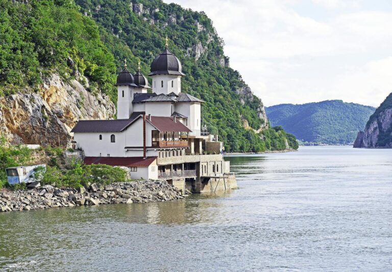 Scenic Orthodox monastery by the Danube River gorge in summer, set against lush green mountains.