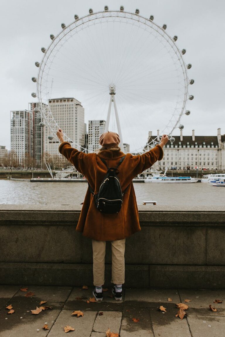 Person with arms raised viewing the London Eye across River Thames in autumn.