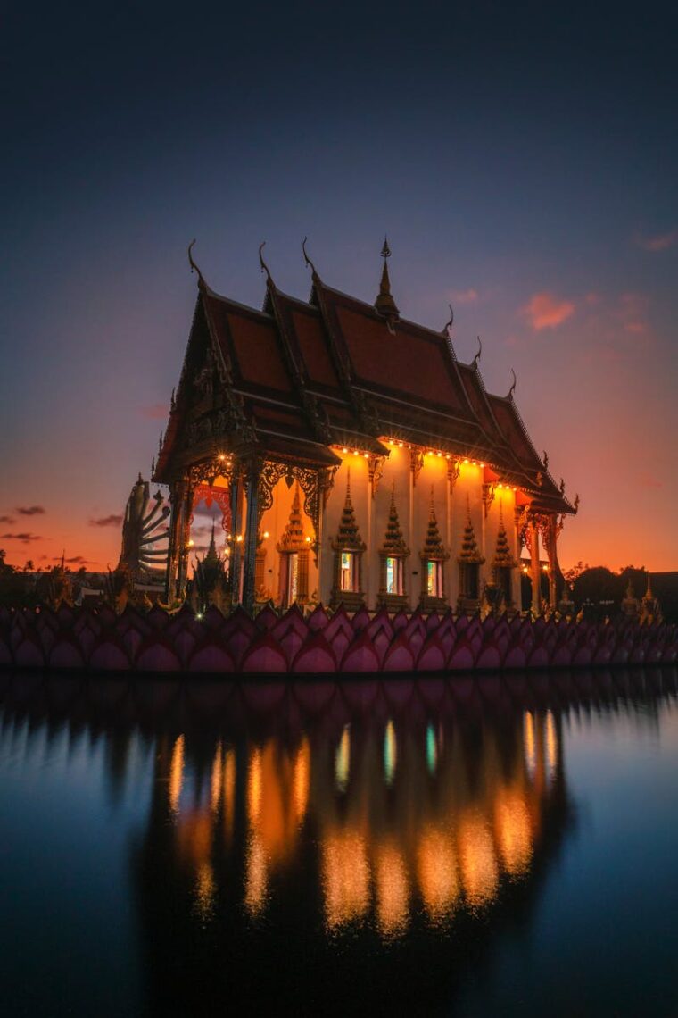 A stunning shot of a beautifully lit Thai temple at sunset, reflecting in the serene water.