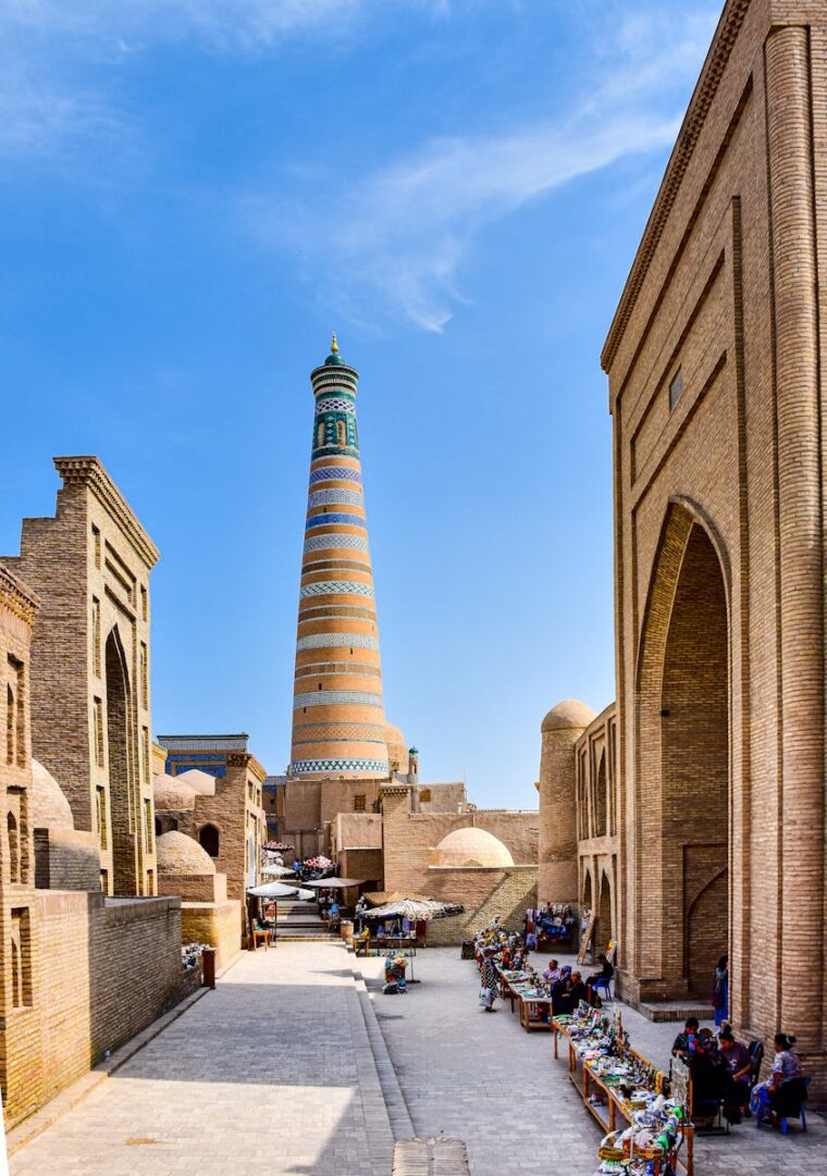 The historic Islam Khoja minaret and its surrounding architecture under a bright blue sky in Khiva, Uzbekistan.