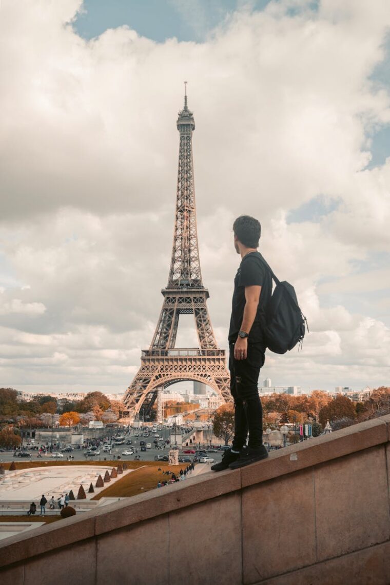 A tourist stands with a backpack admiring the Eiffel Tower in Paris during the day.