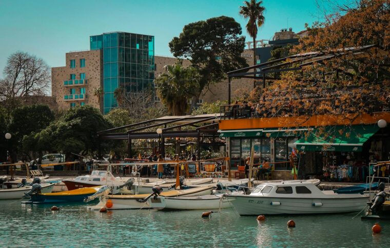 Vibrant marina in Budva with boats docked by bustling cafés, framed by lush greenery.