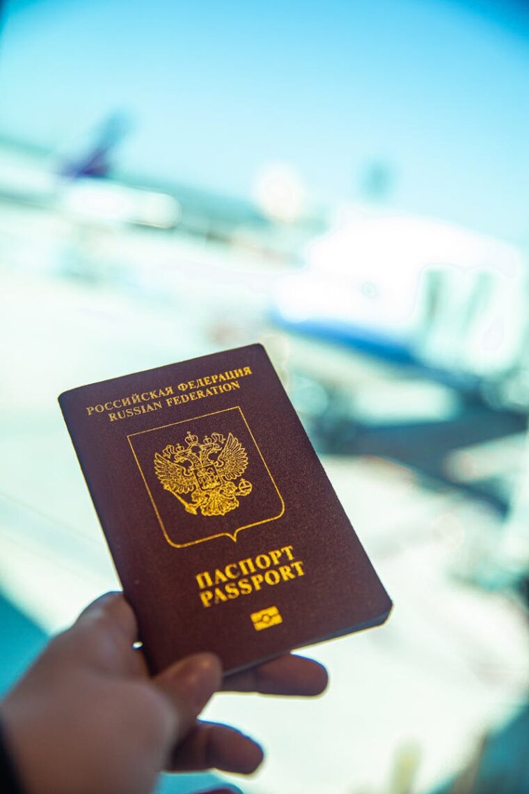 Close-up of a Russian passport being held near an airport gate window with blurred aircraft in the background.