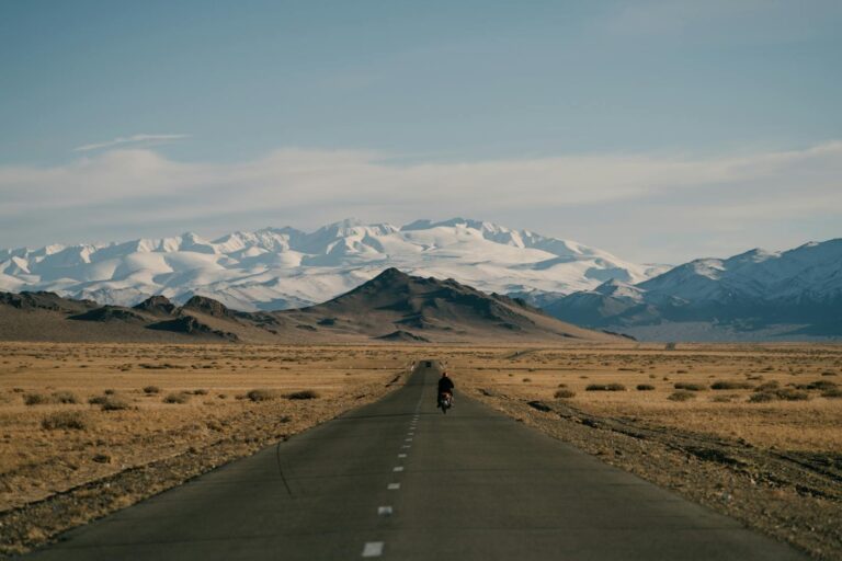 Distant cyclist on a vast highway towards snowcapped mountains in Mongolia.