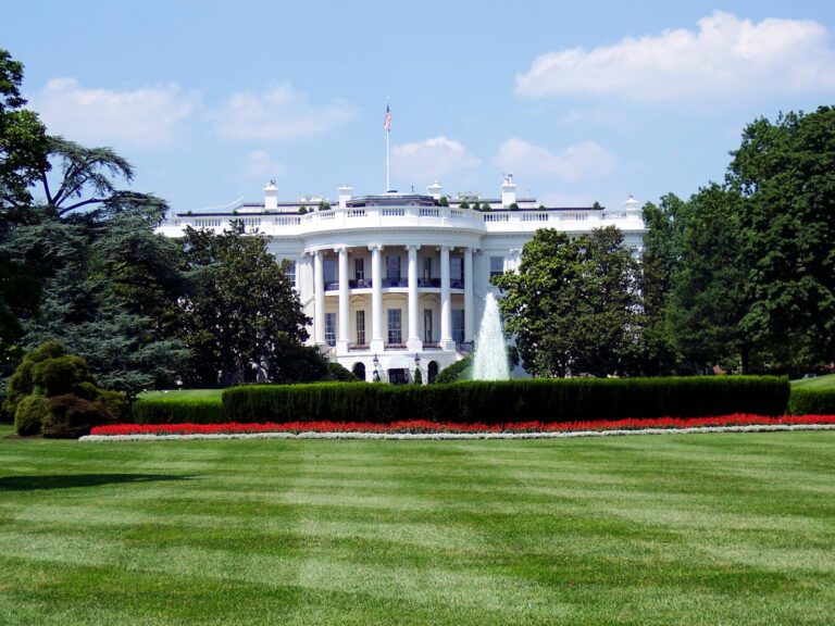 Iconic view of the White House with lush gardens and a central fountain on a sunny day.