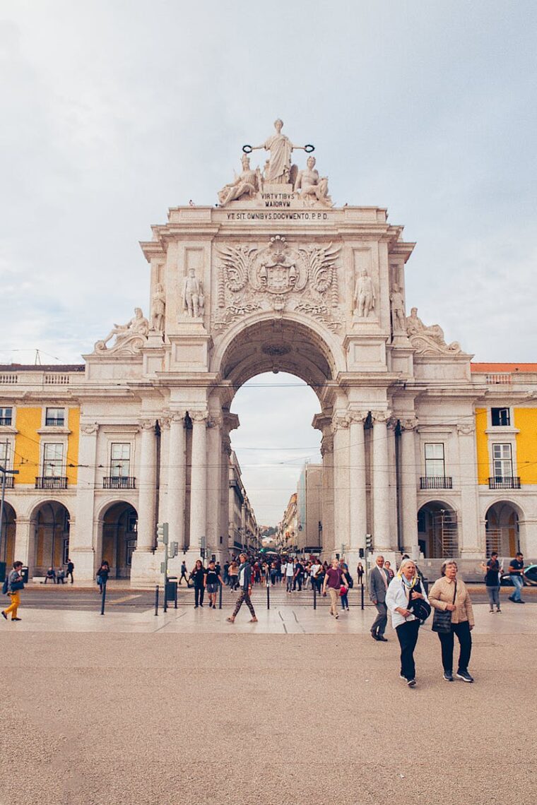 A scenic view of the iconic Rua Augusta Arch in Lisbon, Portugal with people strolling in the plaza.