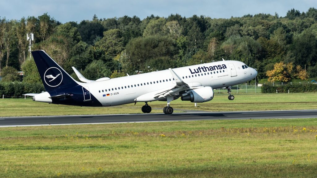 Lufthansa Airbus A320 aircraft touching down on a runway at Hamburg Airport surrounded by greenery.