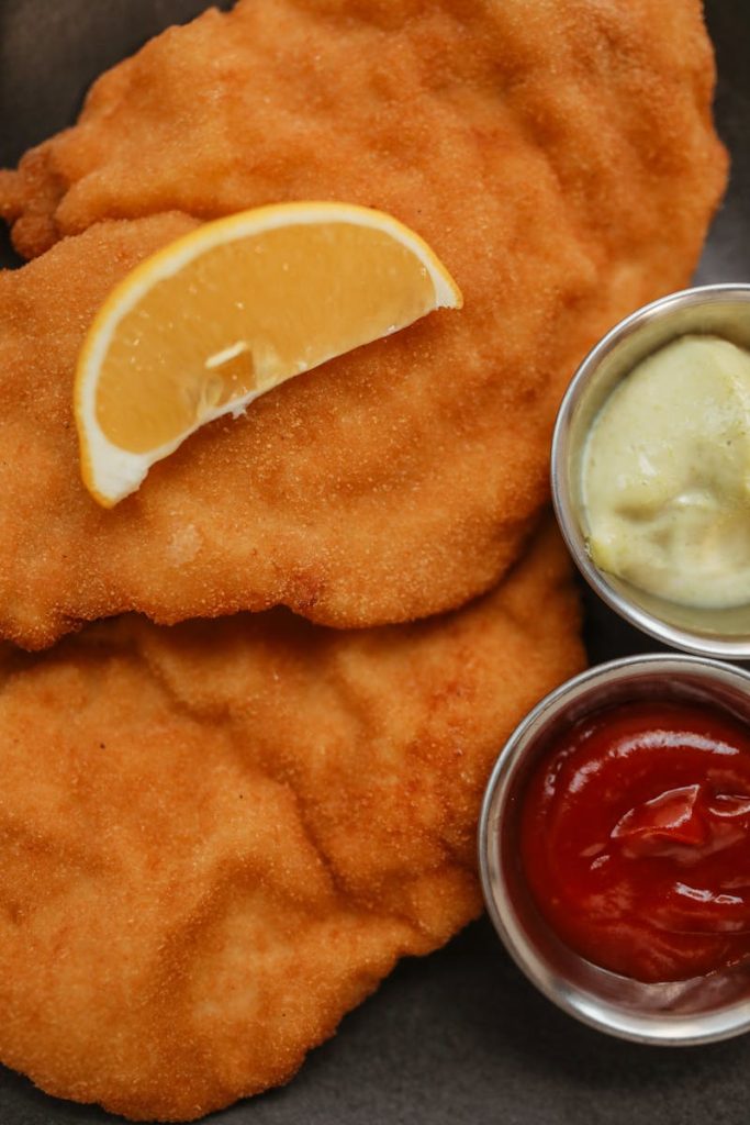 Delicious fried schnitzel served with lemon wedge, mustard, and ketchup.