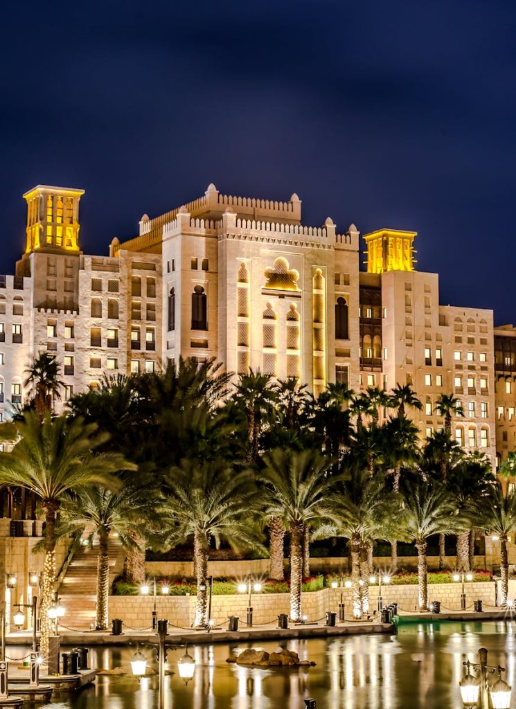 A stunning night view of a luxurious hotel with palm trees reflecting on water in Dubai.